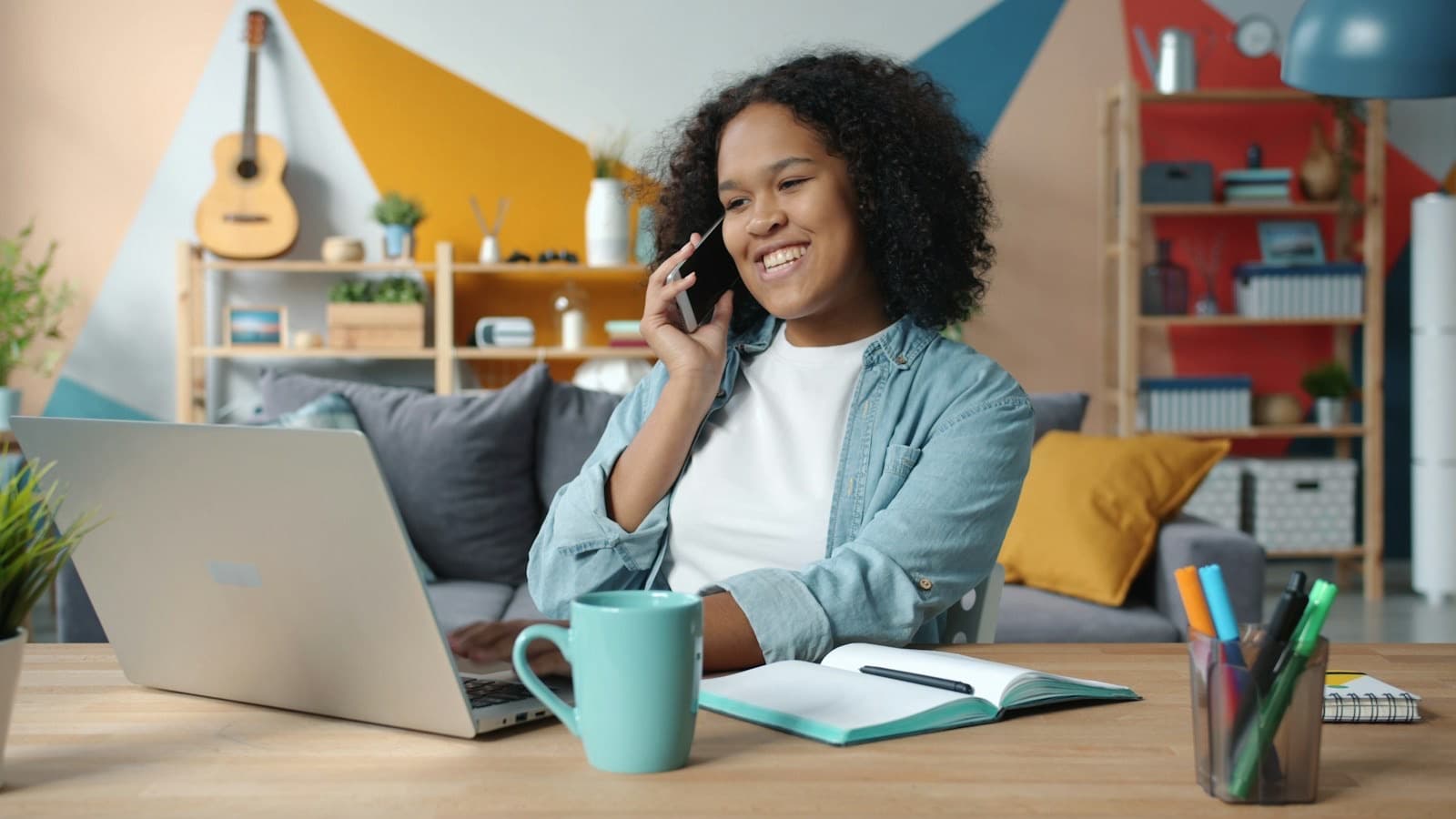 A smiling woman on a phone call at her desk at home